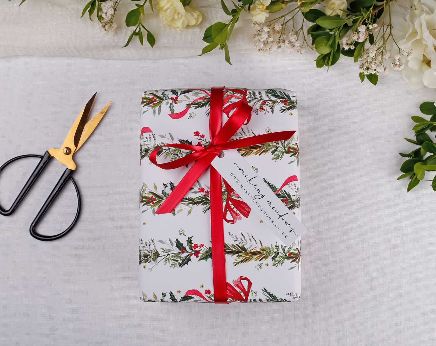 Wrapped gift using Winter Wedding Wrapping Paper adorned with a red ribbon and tag, surrounded by floral accents.