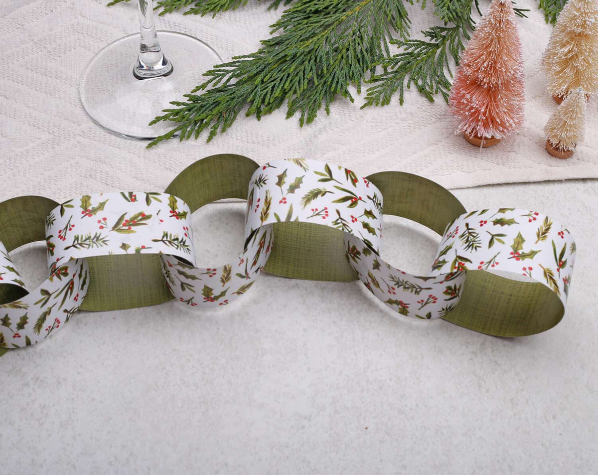Holly Christmas Paper Chains garland displayed on a table with decorative greenery and mini Christmas trees.