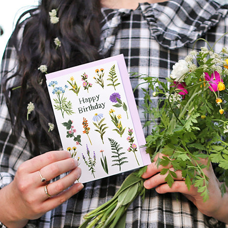 girl holding a making meadows greeting card that says happy birthday and a bunch of flowers