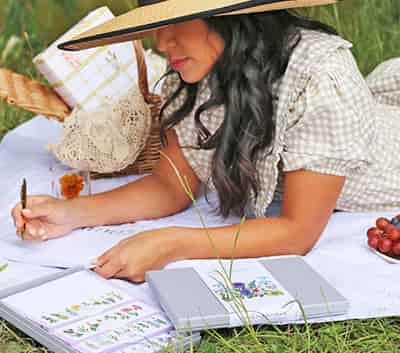 girl writing in her eco friendly writing paper set while on a picnic blanket