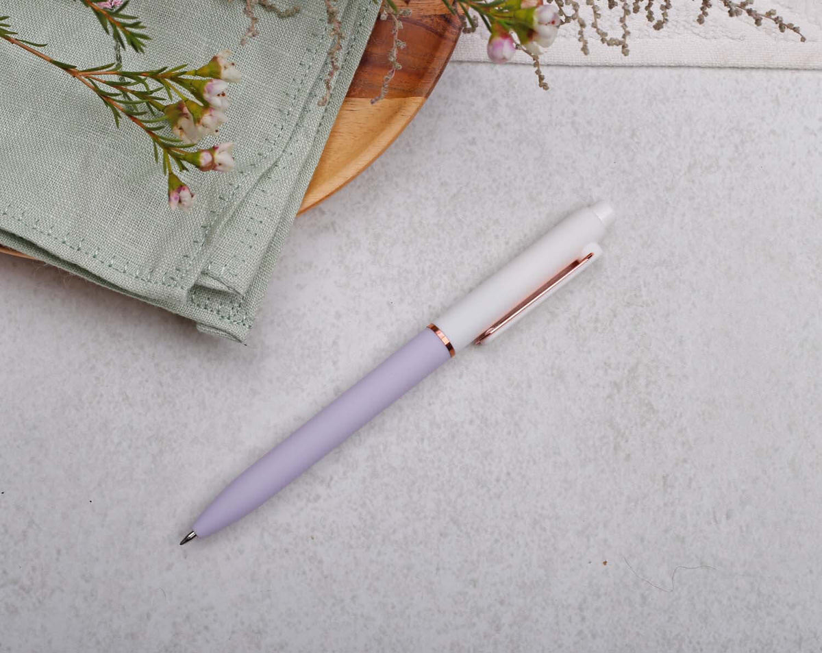 Lilac Gel Pen with rose gold trim placed on a light surface beside greenery and a cloth napkin.