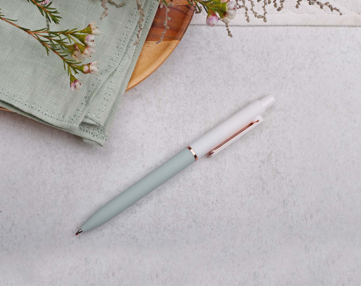 Stylish Green Gel Pen with Rose Gold Trim resting on a table with soft texture fabric and greenery.