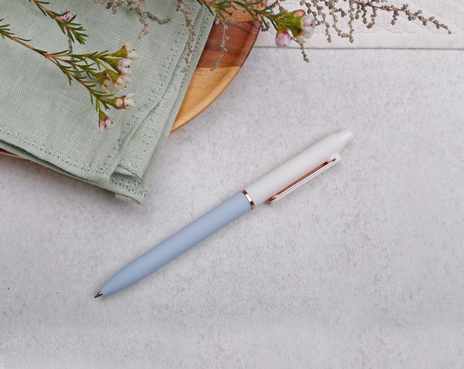 Blue Gel Pen with rose gold trim placed on a textured surface with natural elements nearby.