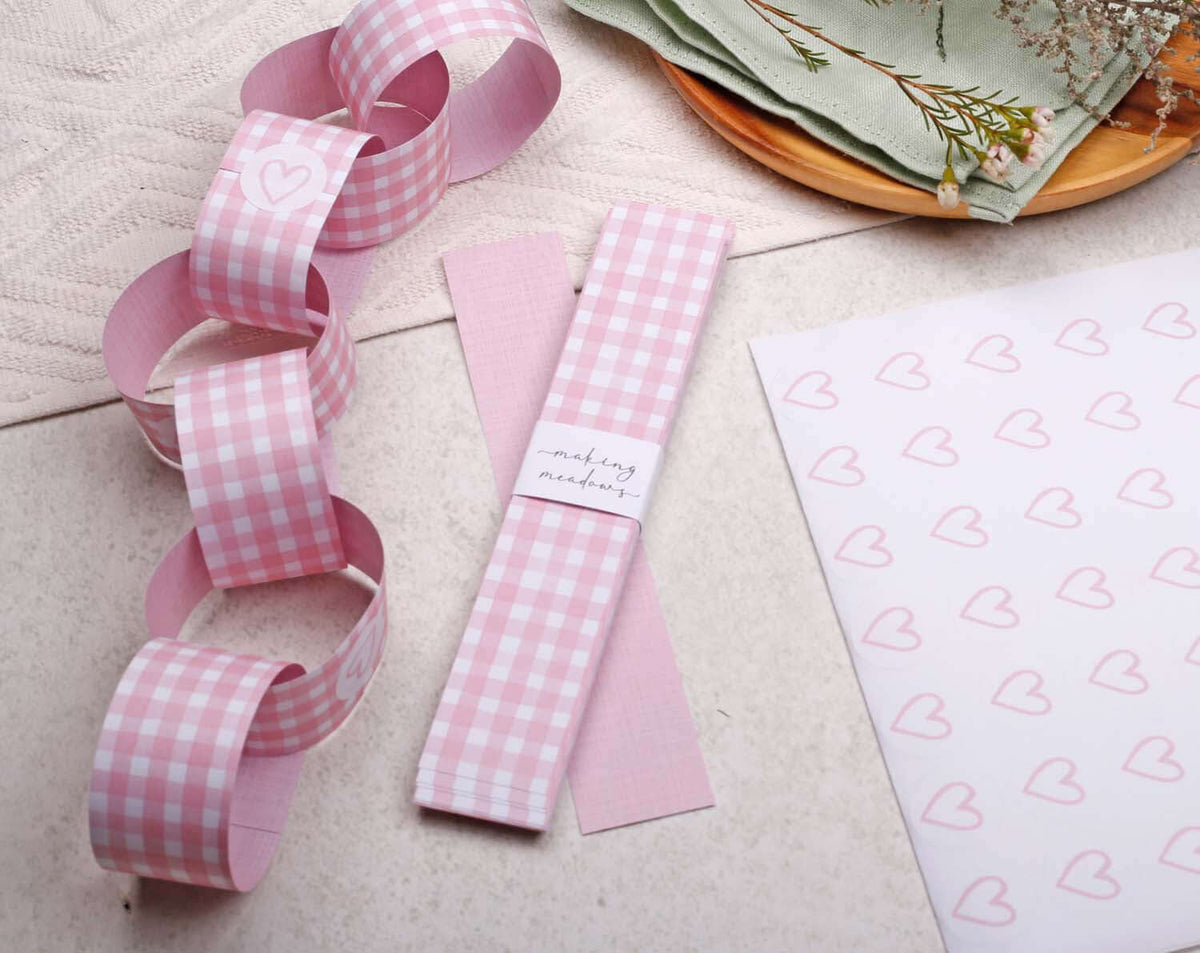 Decorative Pink Gingham Paper Chains featuring heart designs on a table with green napkins and patterned paper.