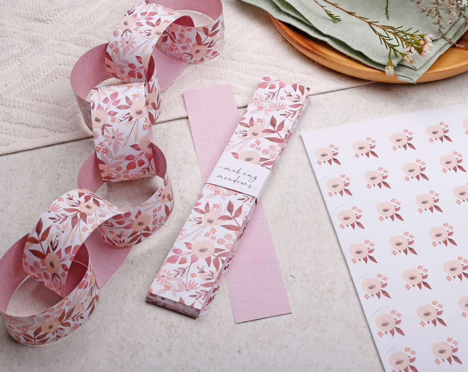 Pink Floral Paper Chains Garland displayed with floral paper and fabric, perfect for festive decorations.