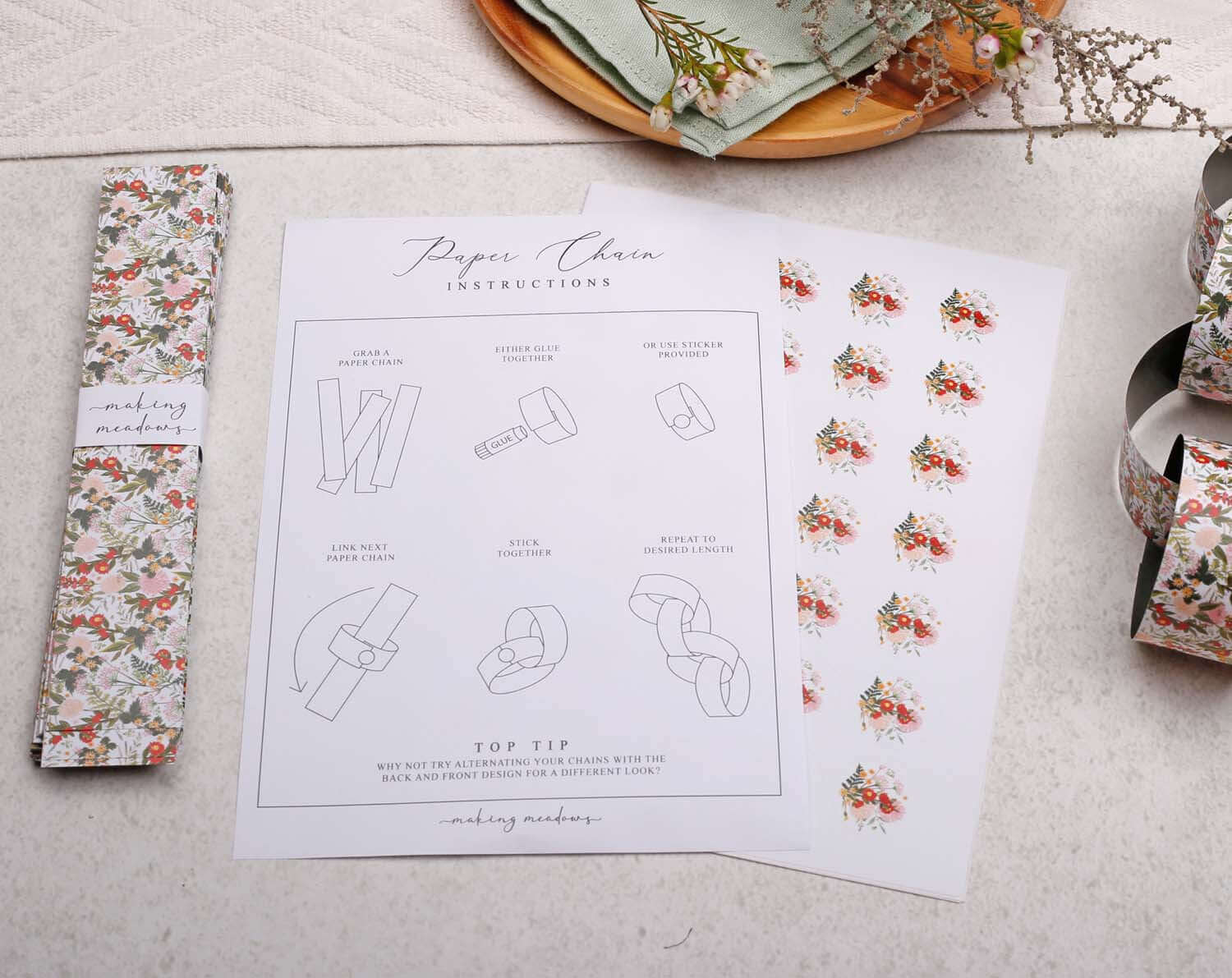 Boho Floral Paper Chains instructions sheet with step-by-step guide and floral paper chain strips laid out on a light surface.