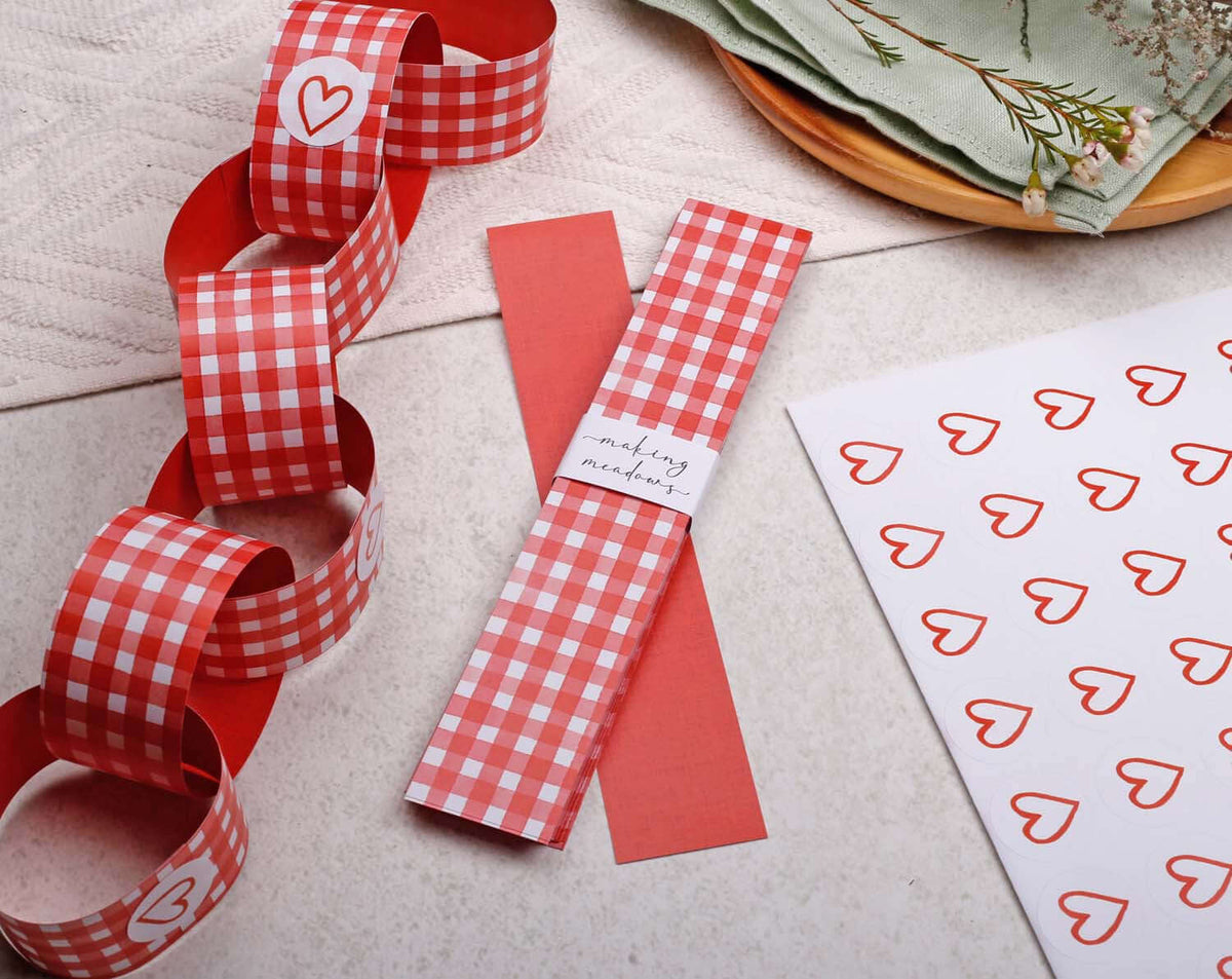 Red Gingham Paper Chains garland with heart patterns and red paper on a table surface.