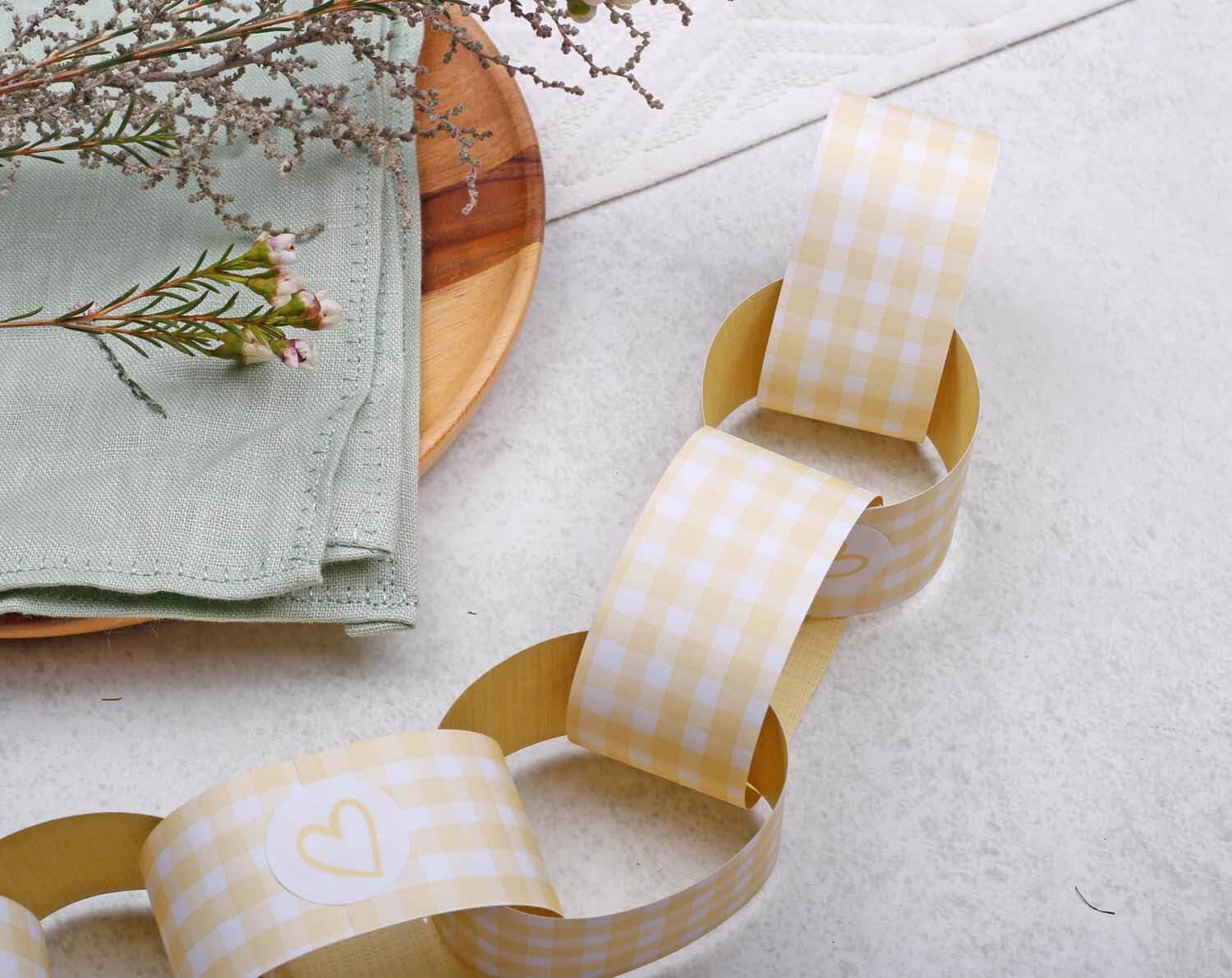 Yellow Gingham Paper Chains Garland displayed on a table with natural decor items, perfect for festive occasions.
