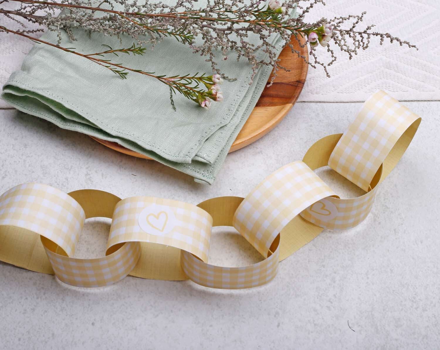 Yellow Gingham Paper Chains Garland featuring yellow and white checkered design with a sprig of flowers and napkins.