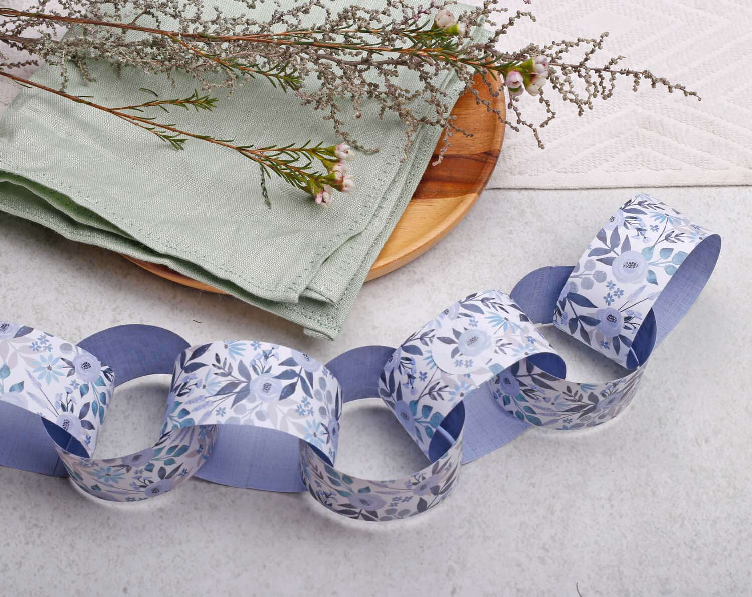 Blue Floral Paper Chains garland displayed on a wooden platter with greenery and napkins.