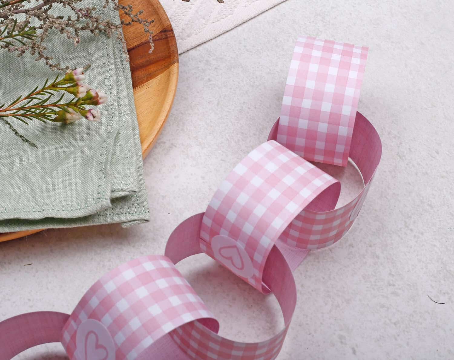Pink Gingham Paper Chains displayed on a table with flowers and a napkin, perfect for party decor.
