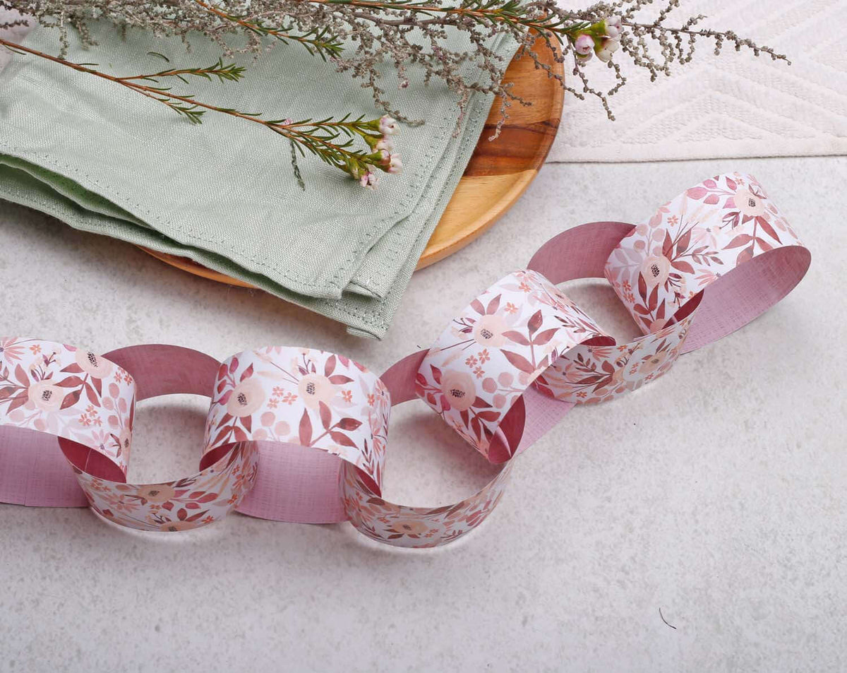Pink Floral Paper Chains Garland displayed with green napkin and vase, perfect for decorating events.