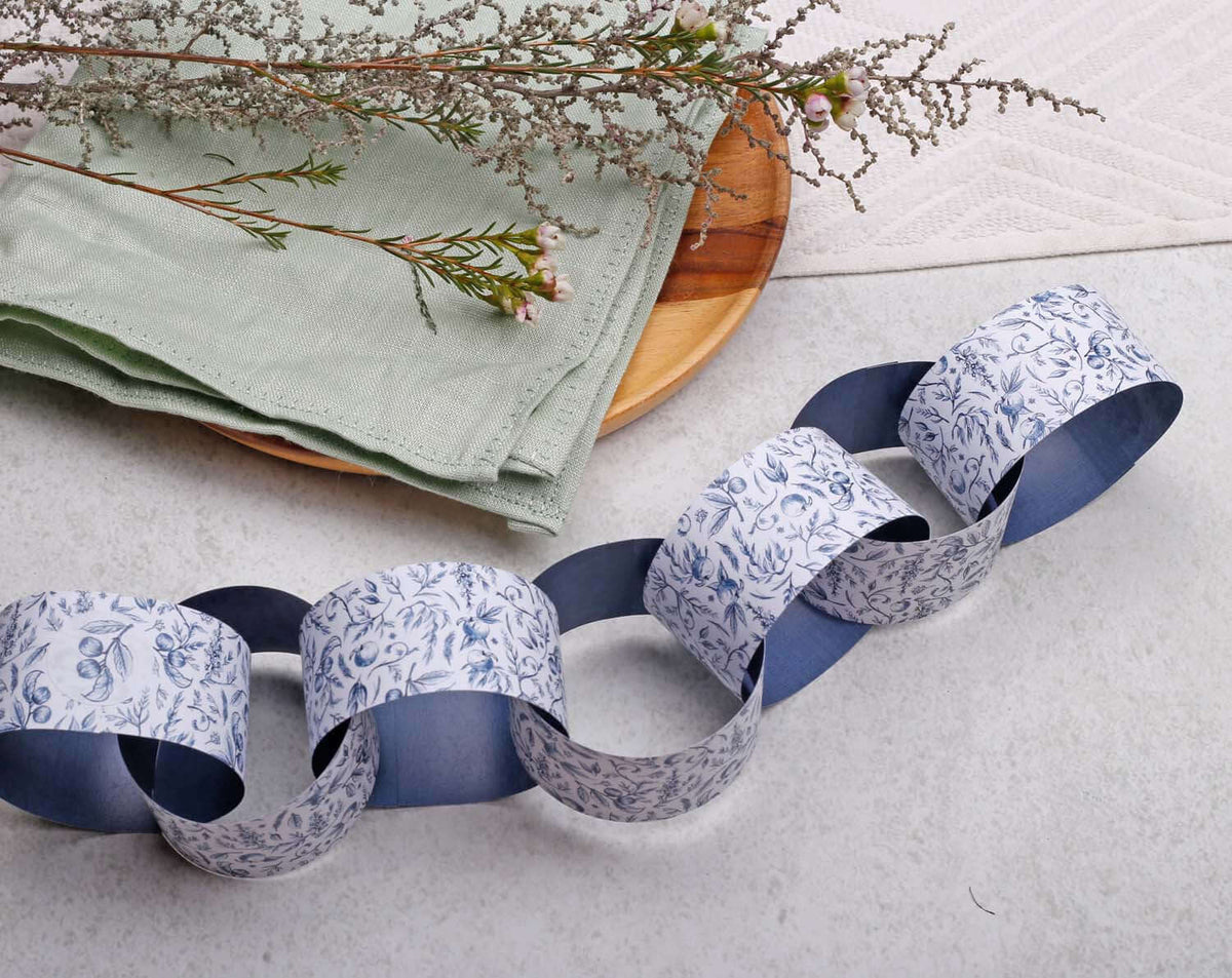 Blue Garden Paper Chains Garland displayed on a rustic setting with green linens and decorative twigs.