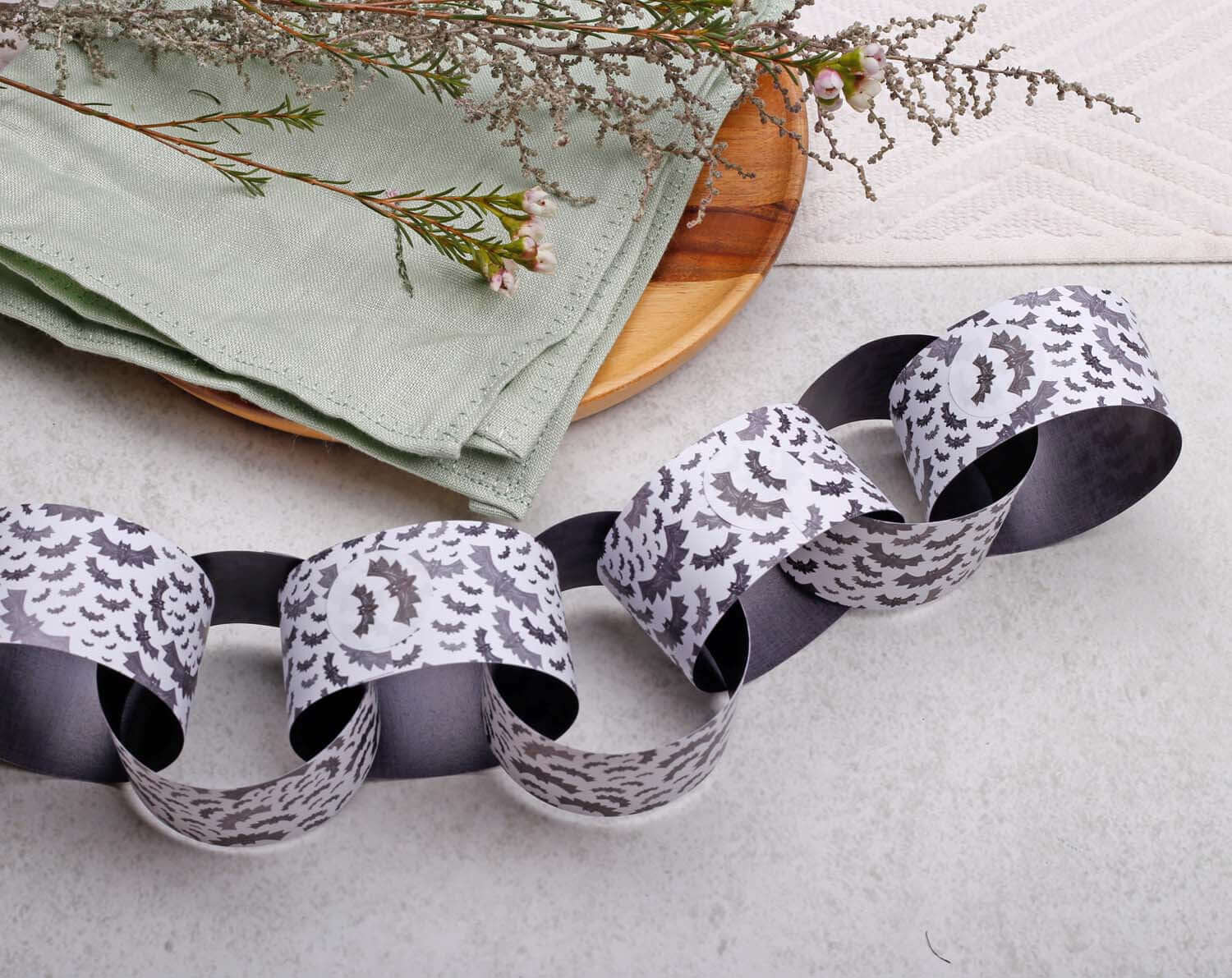 Decorative Bat Halloween Paper Chains Garland displayed on a table with a green napkin and wooden plate.