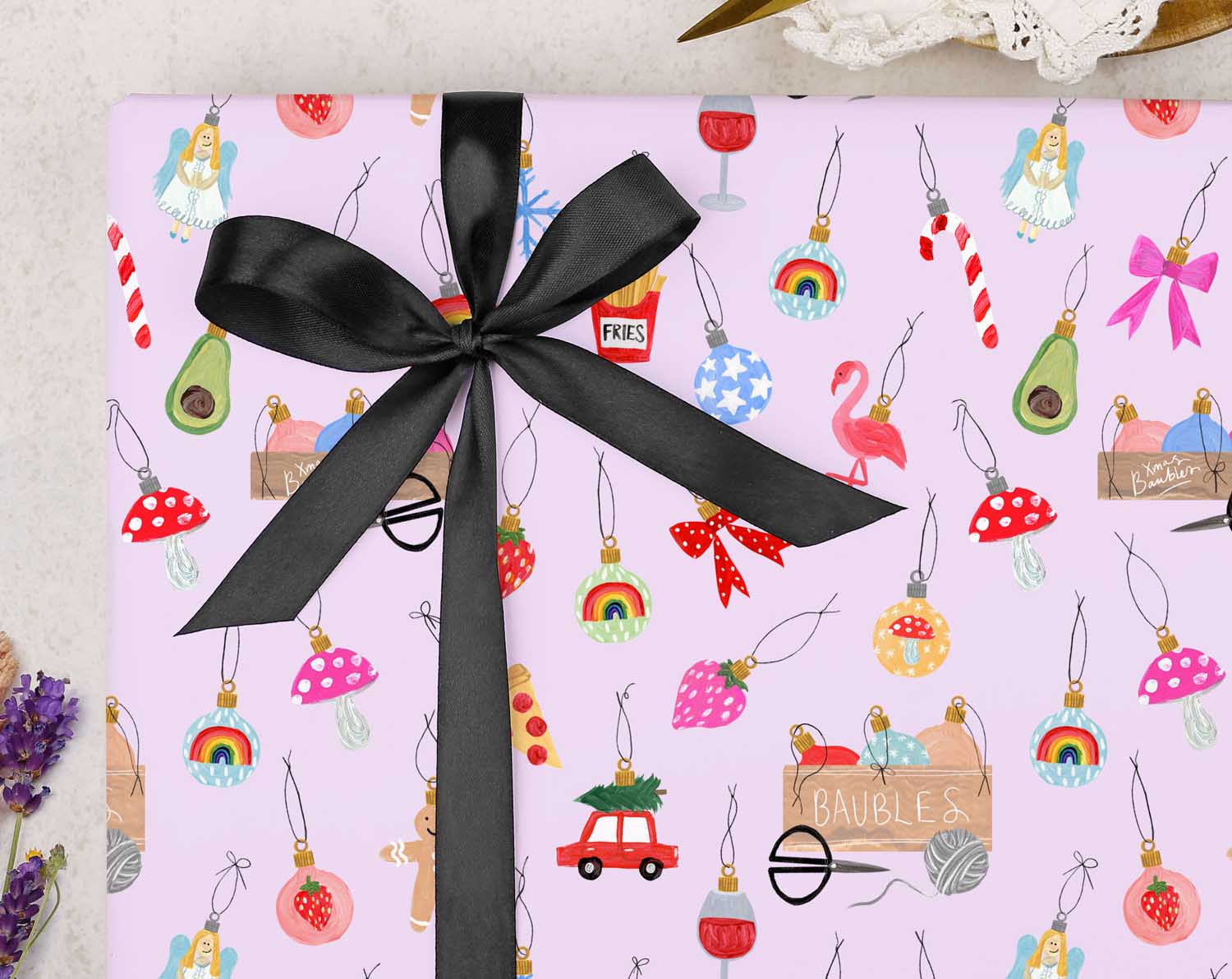 festive Christmas wrapping paper is filled with Christmas Ornaments on a lilac background